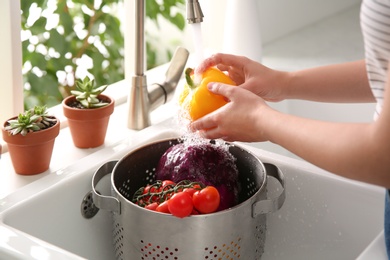 Photo of Woman washing fresh bell pepper in kitchen sink, closeup
