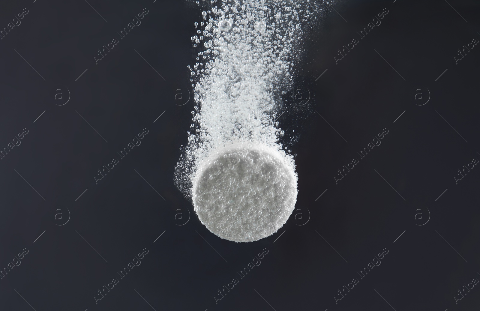 Photo of Effervescent pill dissolving in water on dark background, closeup