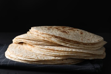 Photo of Many tasty homemade tortillas on black wooden table, closeup