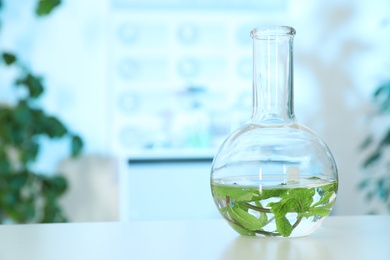 Glass flask with leaves on table in laboratory, space for text. Plant chemistry