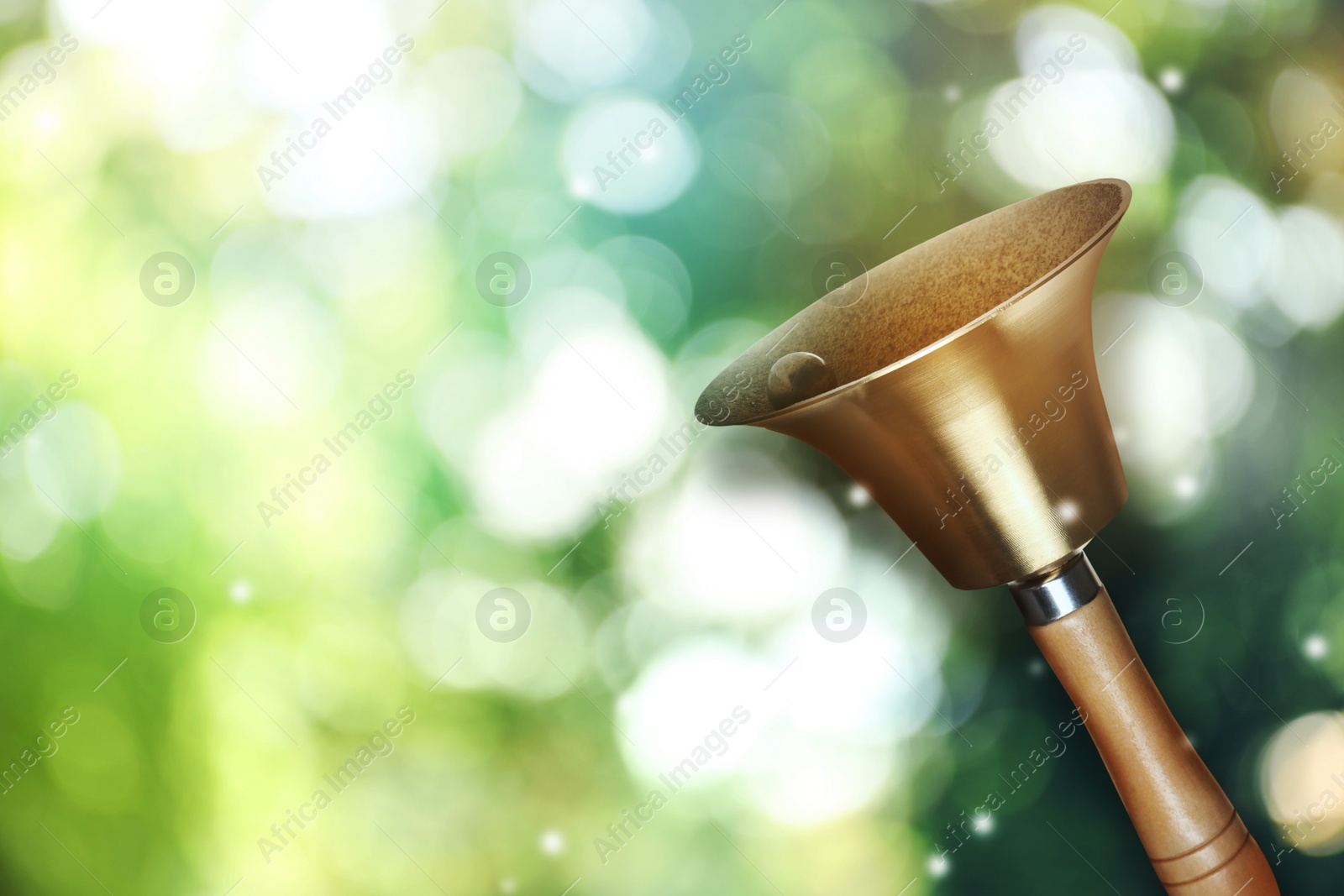 Image of Shiny school bell with wooden handle outdoors, space for text. Bokeh effect