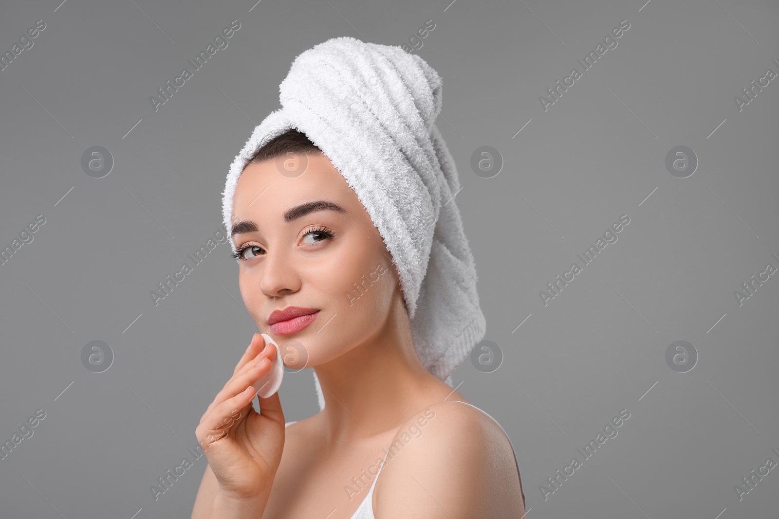 Photo of Beautiful woman in terry towel removing makeup with cotton pad on gray background, space for text