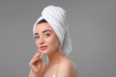 Photo of Beautiful woman in terry towel removing makeup with cotton pad on gray background, space for text