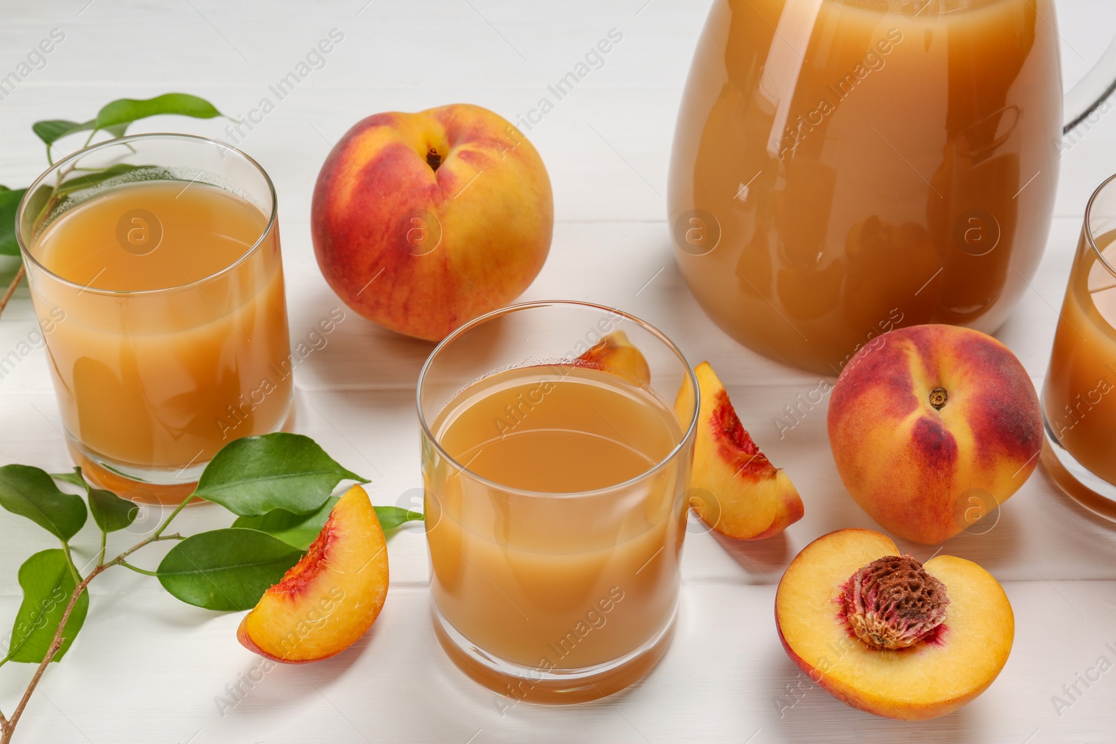 Photo of Delicious peach juice, fresh fruits and leaves on white wooden table