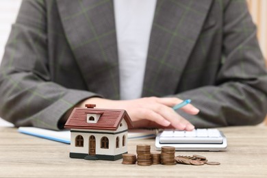 Photo of Woman with house model and stacked coins at wooden table, closeup