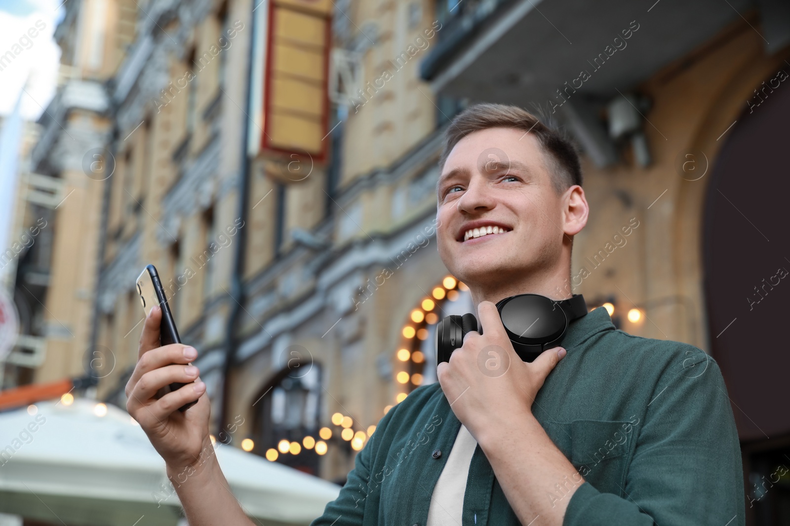 Photo of Smiling man with headphones using smartphone outdoors, low angle view. Space for text