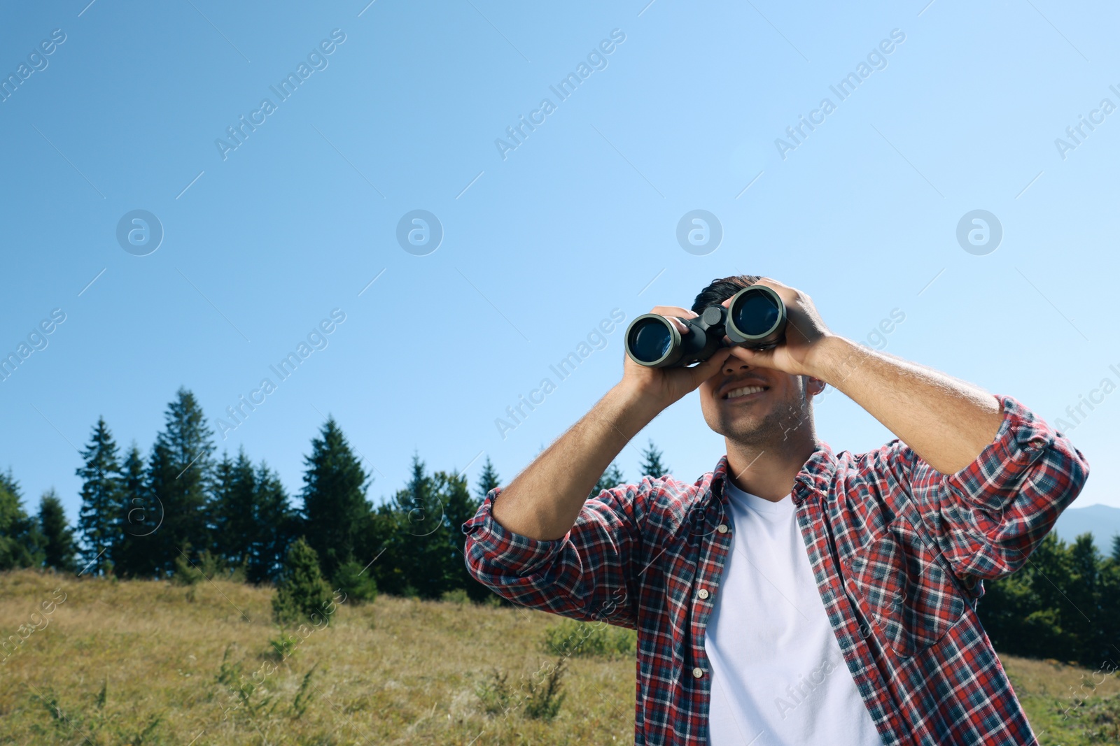 Photo of Man looking through binoculars outdoors on sunny day