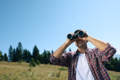 Man looking through binoculars outdoors on sunny day