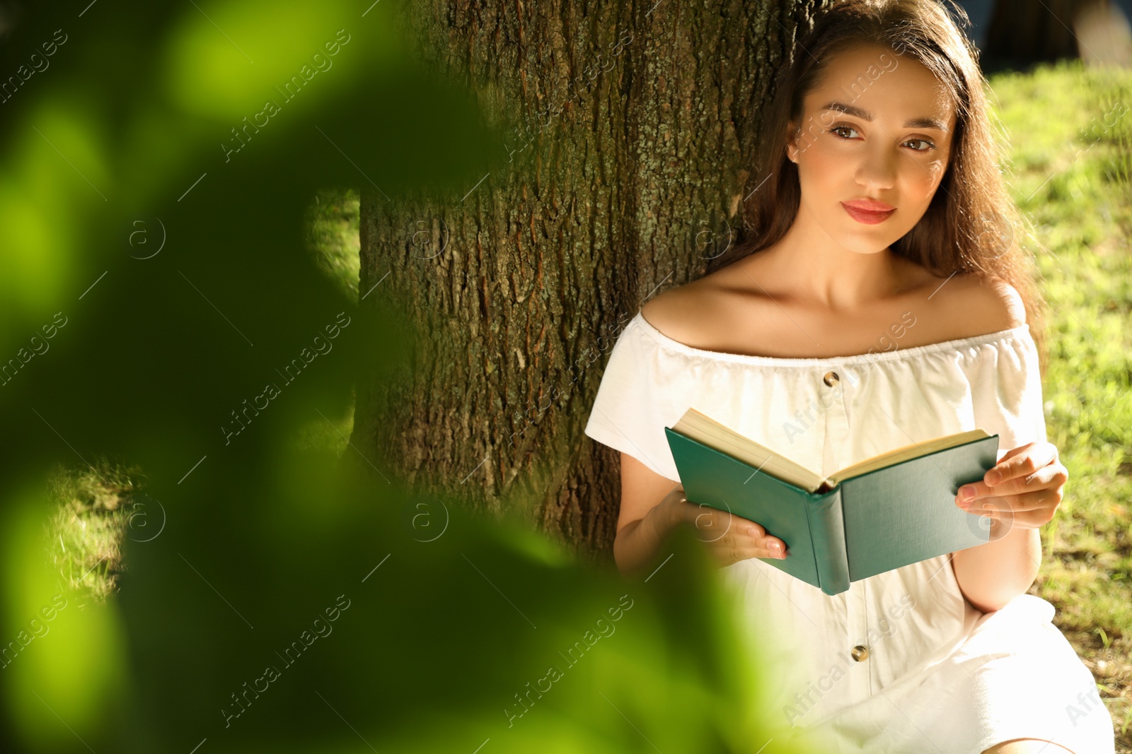 Photo of Beautiful young woman reading book near tree in park