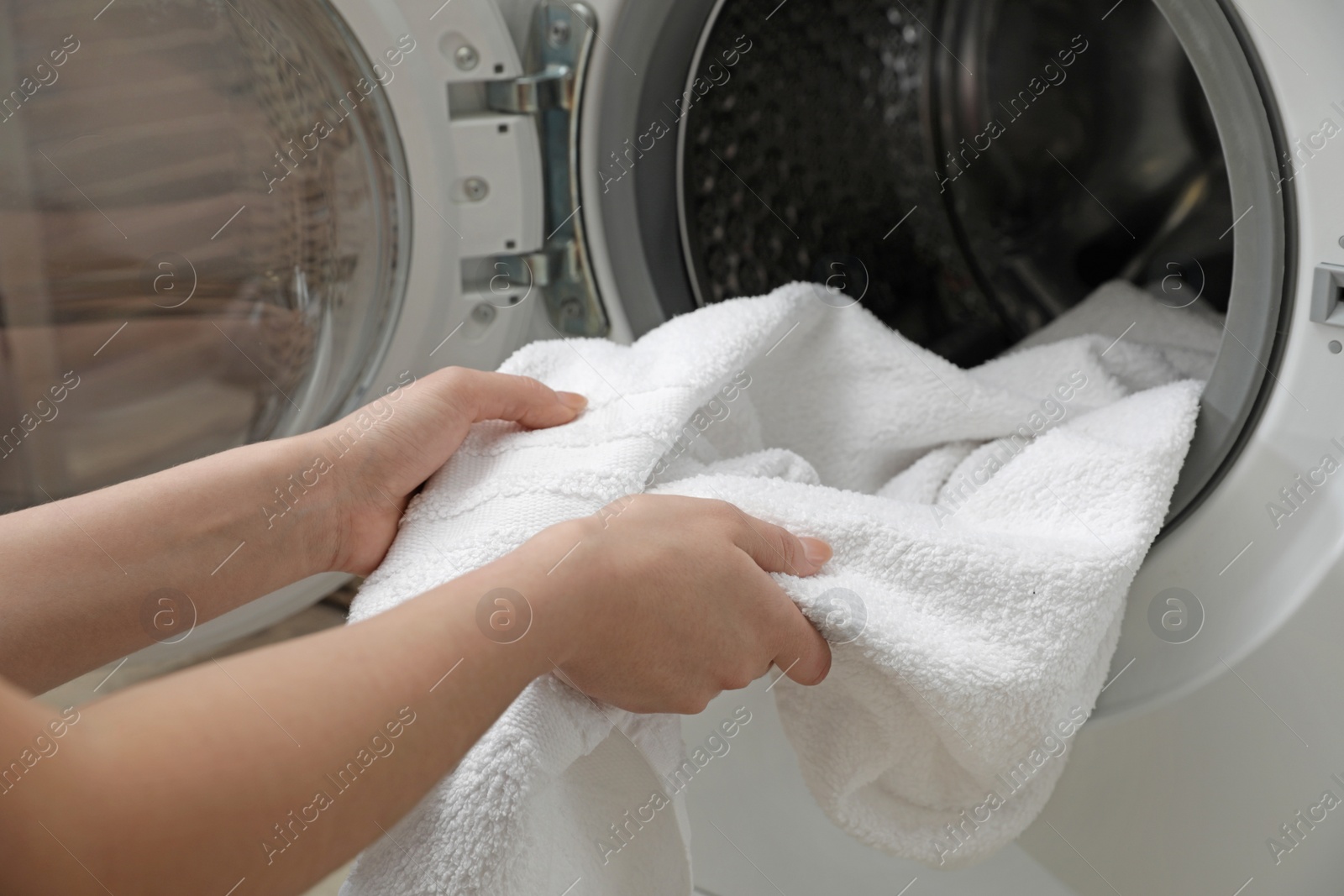 Photo of Woman taking clean towel from washing machine in laundry room, closeup