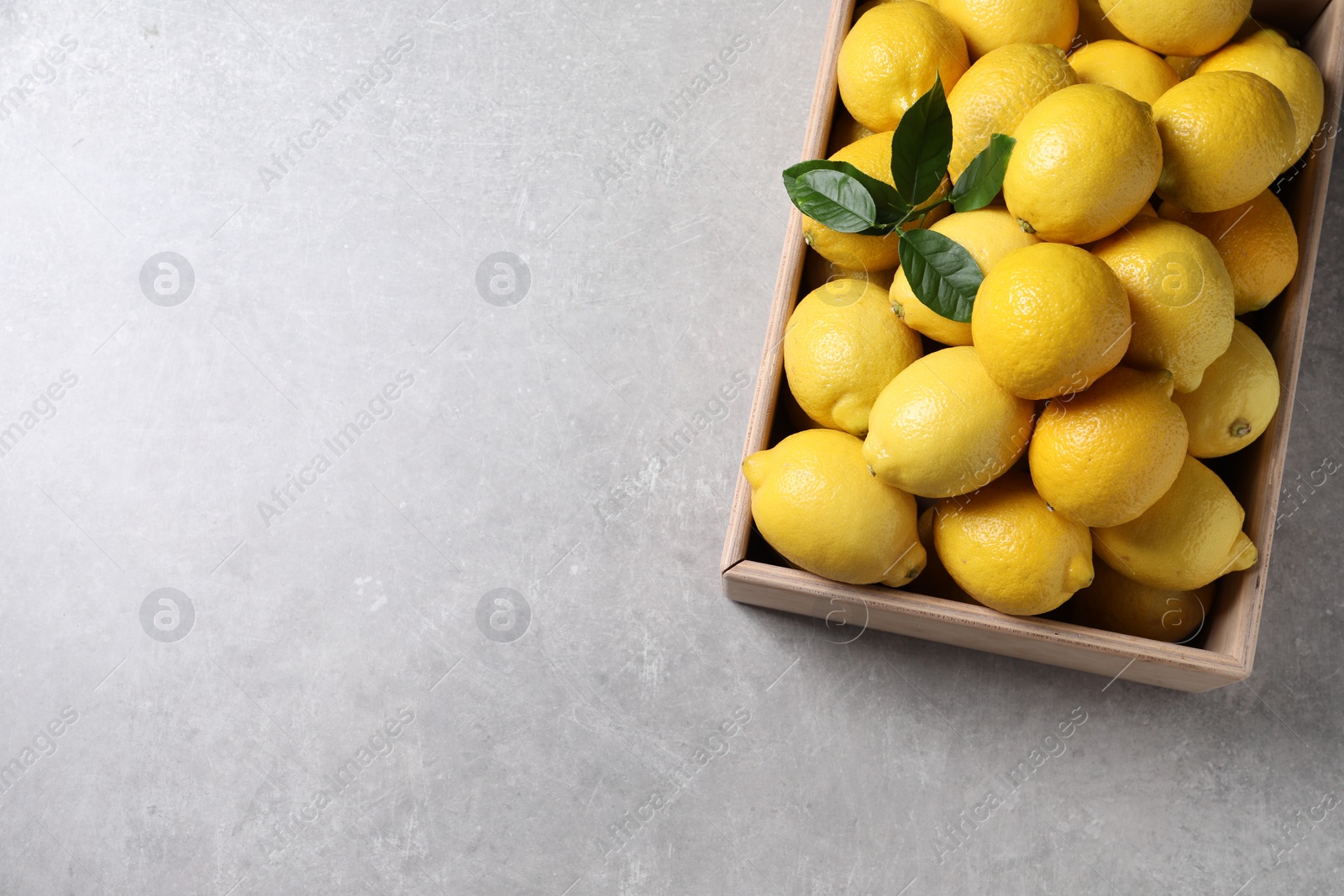 Photo of Fresh lemons in wooden crate on grey table, top view. Space for text