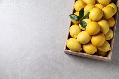Fresh lemons in wooden crate on grey table, top view. Space for text