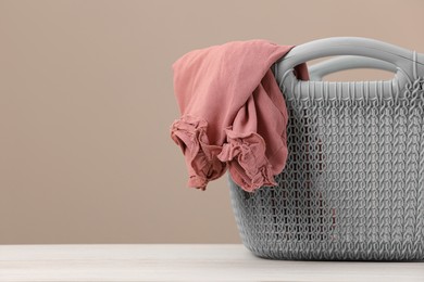 Photo of Plastic laundry basket with clothes near beige wall. Space for text