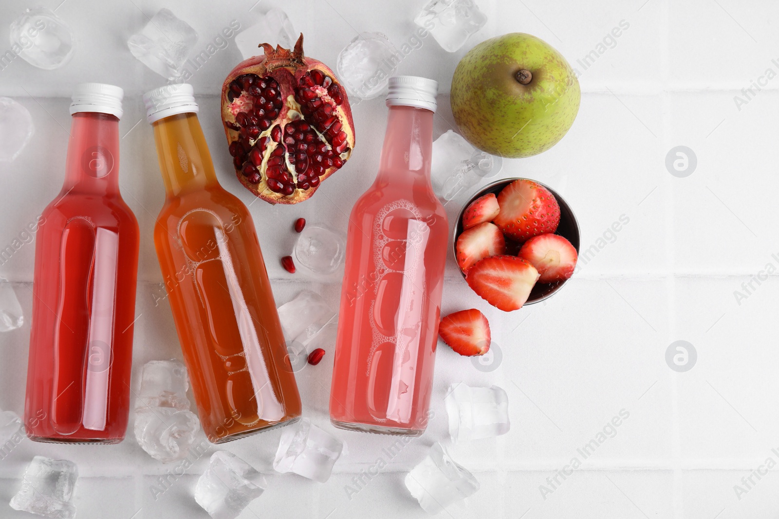 Photo of Tasty kombucha in glass bottles, fresh fruits and ice on white table, flat lay. Space for text