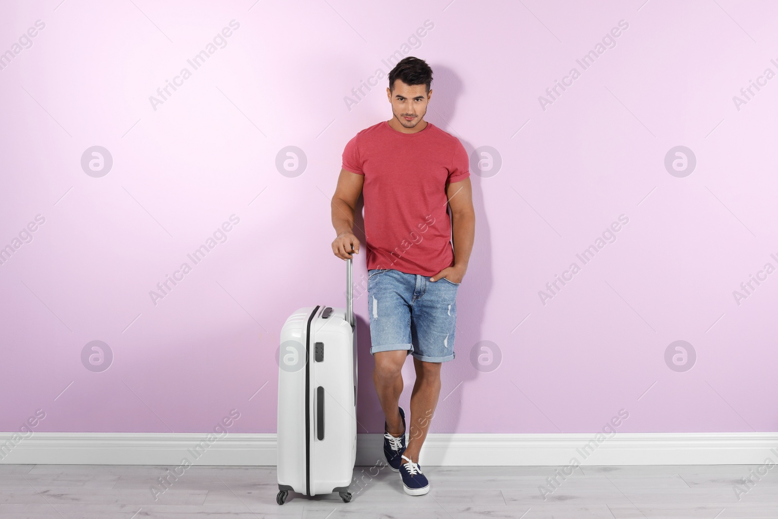 Photo of Young man with suitcase on color wall background