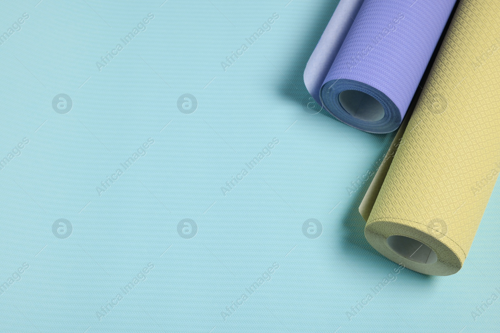 Image of Colorful wallpaper rolls on light blue background, above view. Space for text