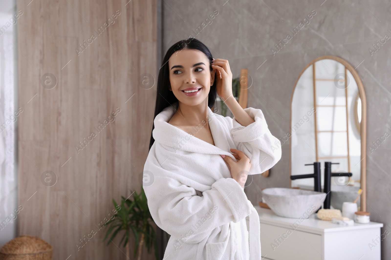 Photo of Beautiful young woman wearing soft white robe in bathroom