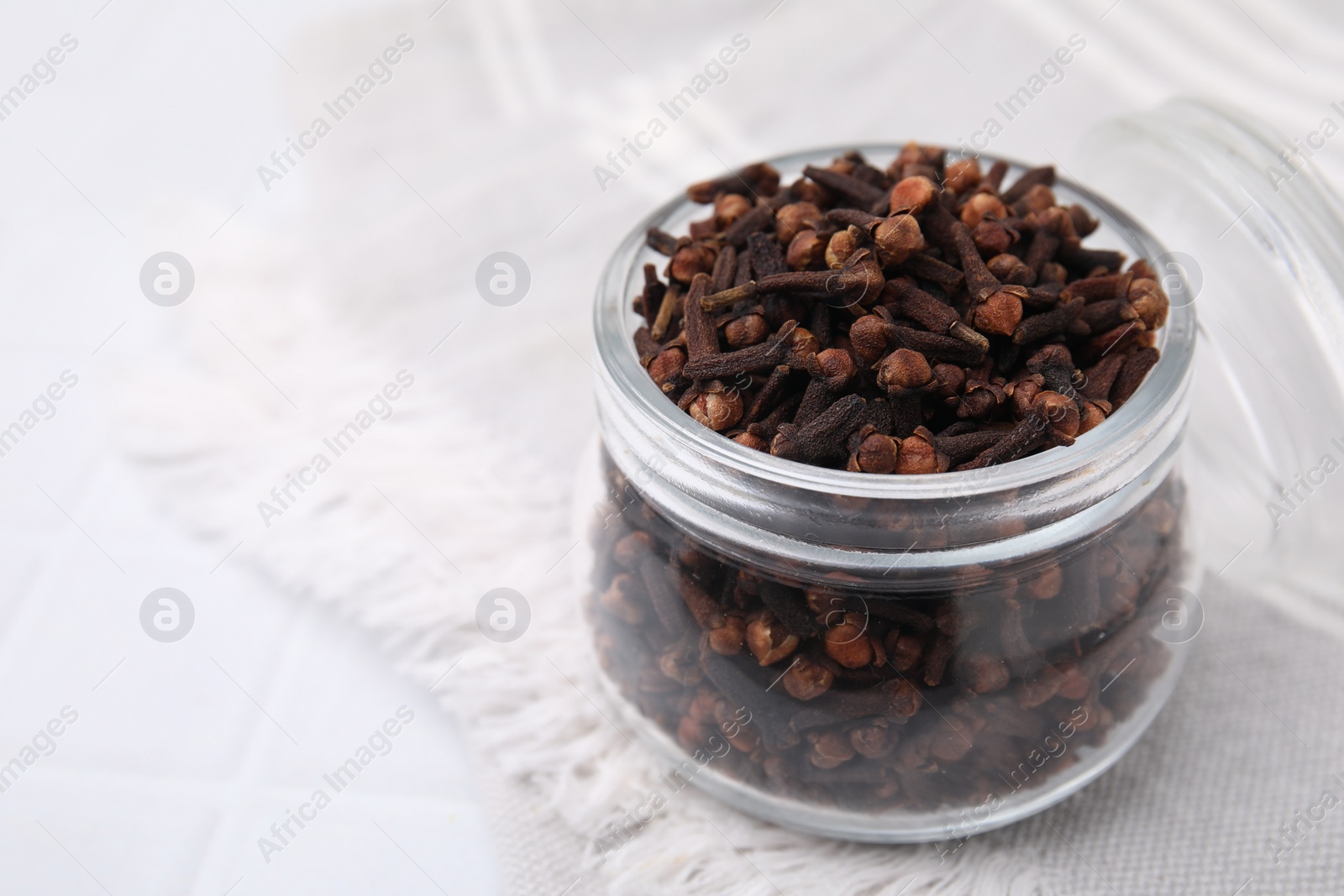 Photo of Aromatic cloves in glass jar on white table, closeup. Space for text