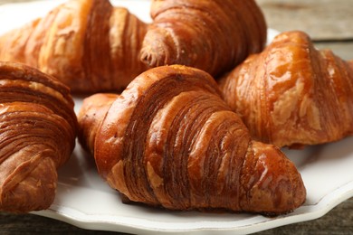 Photo of Plate with tasty croissants on wooden table, closeup