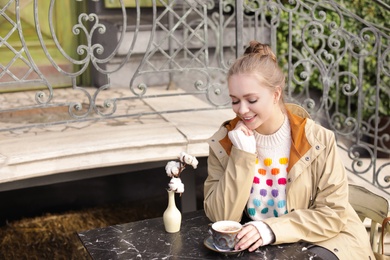 Young woman enjoying tasty coffee at table outdoors