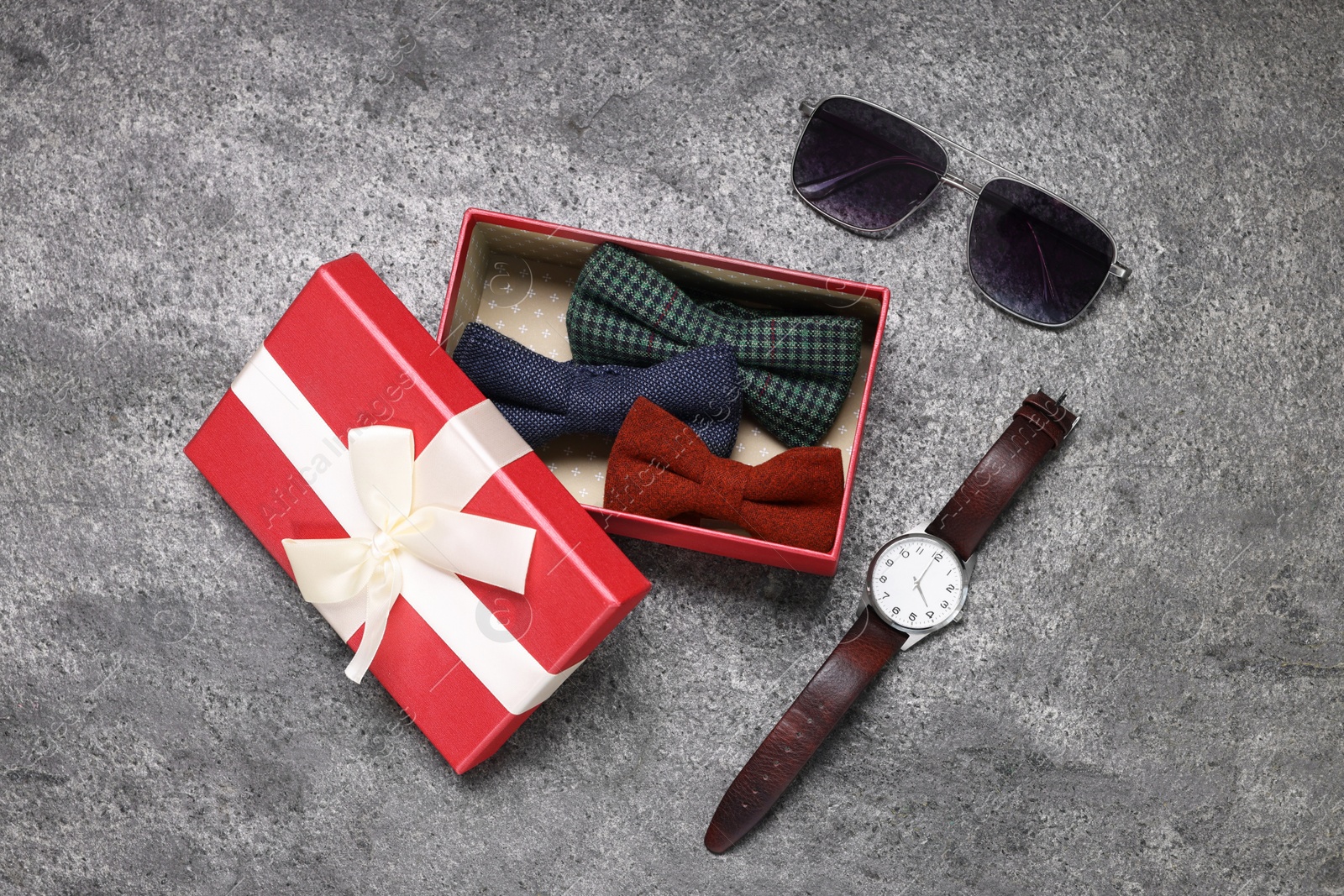 Photo of Stylish color bow ties in gift box, wristwatch and sunglasses on grey textured background, flat lay