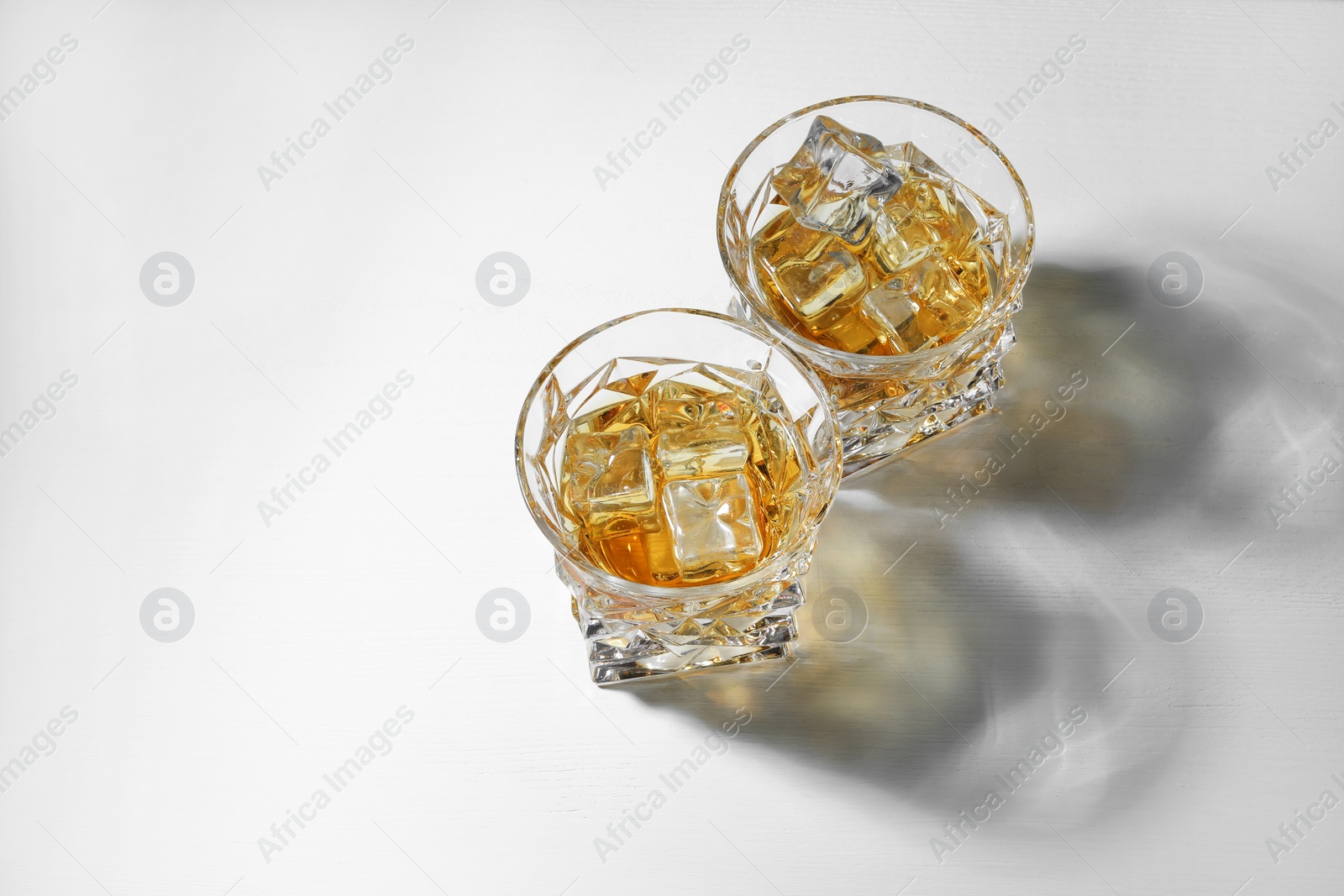 Photo of Whiskey with ice cubes in glasses on white table, above view. Space for text