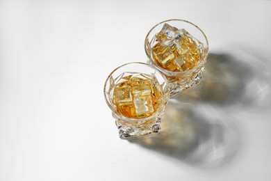 Photo of Whiskey with ice cubes in glasses on white table, above view. Space for text