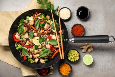 Photo of Stir-fry. Tasty noodles with meat in wok, chopsticks and ingredients on grey textured table, flat lay