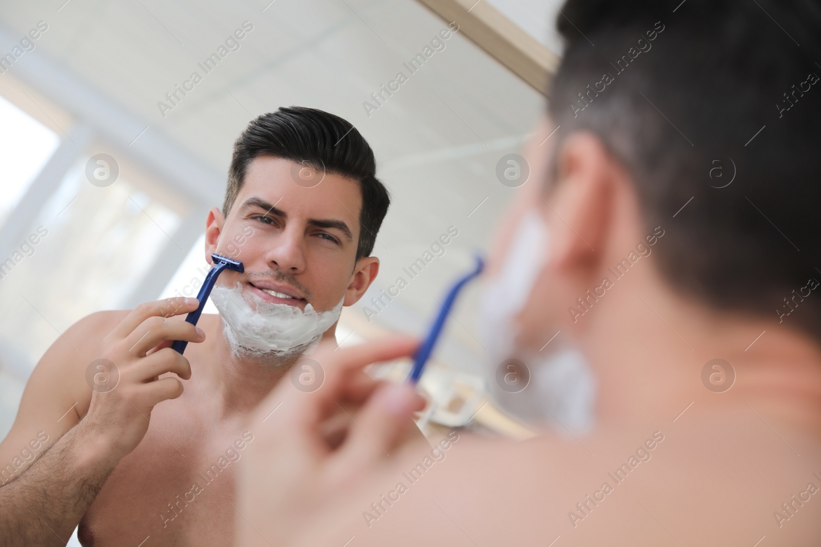 Photo of Handsome man shaving near mirror in bathroom