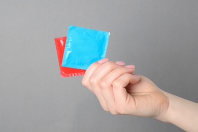 Woman holding condoms on grey background, closeup