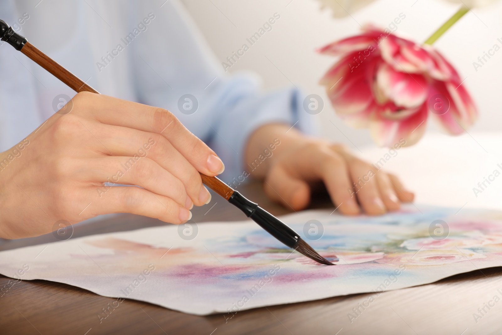 Photo of Woman painting flowers with watercolor at wooden table indoors, closeup. Creative artwork