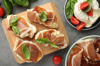 Photo of Tasty sandwiches with cured ham, tomatoes and arugula on grey table, flat lay