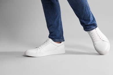 Man wearing stylish white sneakers on grey background, closeup