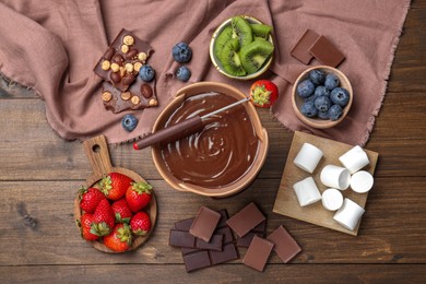 Photo of Fondue pot with melted chocolate, marshmallows, fresh kiwi, different berries and fork on wooden table, flat lay