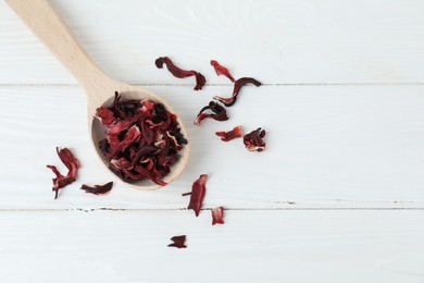Photo of Hibiscus tea. Spoon with dried roselle calyces on white wooden table, top view. Space for text
