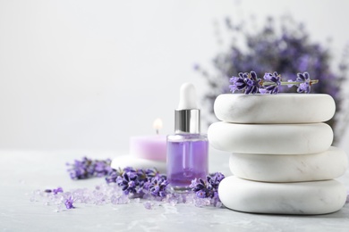 Photo of Spa stones, natural cosmetic oil and lavender flowers on grey table, space for text