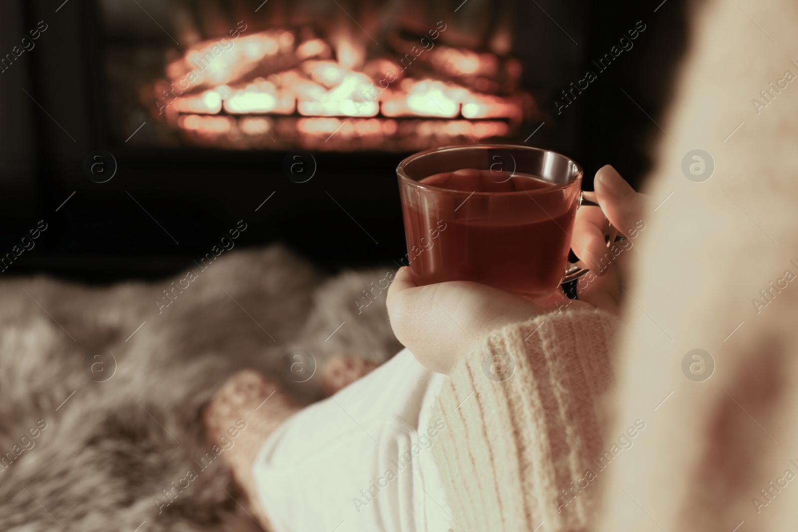 Photo of Woman with cup of tea resting near fireplace at home, closeup