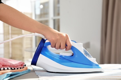 Woman ironing clothes on board indoors. Household chores