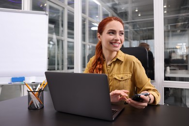 Happy woman with smartphone working on laptop at black desk in office