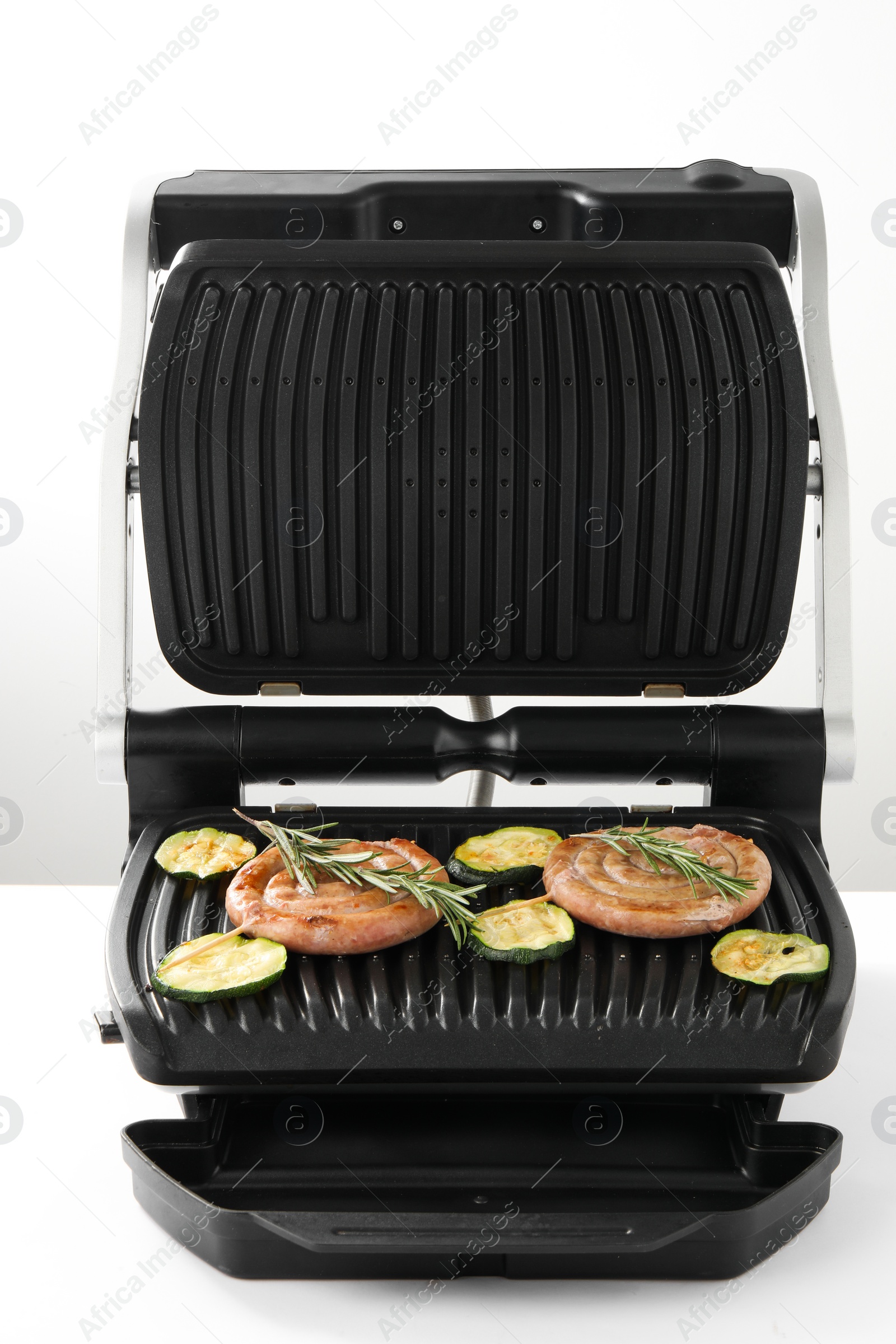 Photo of Electric grill with homemade sausages, zucchini and rosemary isolated on white