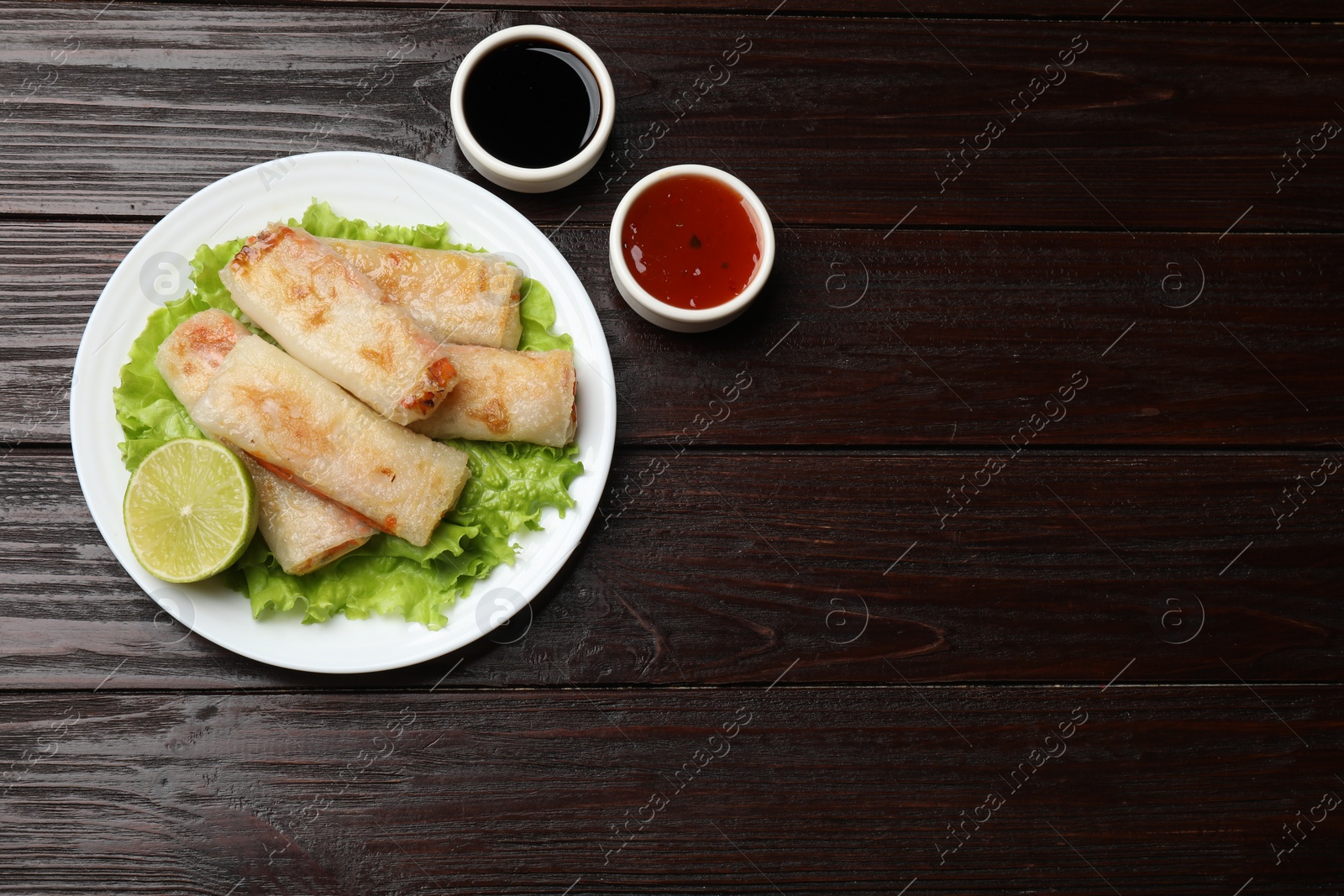 Photo of Delicious fried spring rolls served on wooden table, flat lay. Space for text