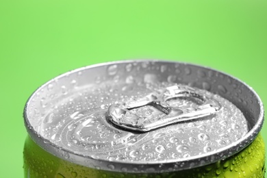 Photo of Aluminum can of beverage covered with water drops on green background, closeup