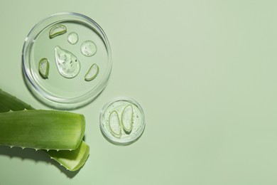 Photo of Cut aloe vera and drops of cosmetic gel on light green background, flat lay. Space for text