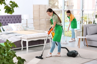 Photo of Team of professional janitors in uniform cleaning bedroom