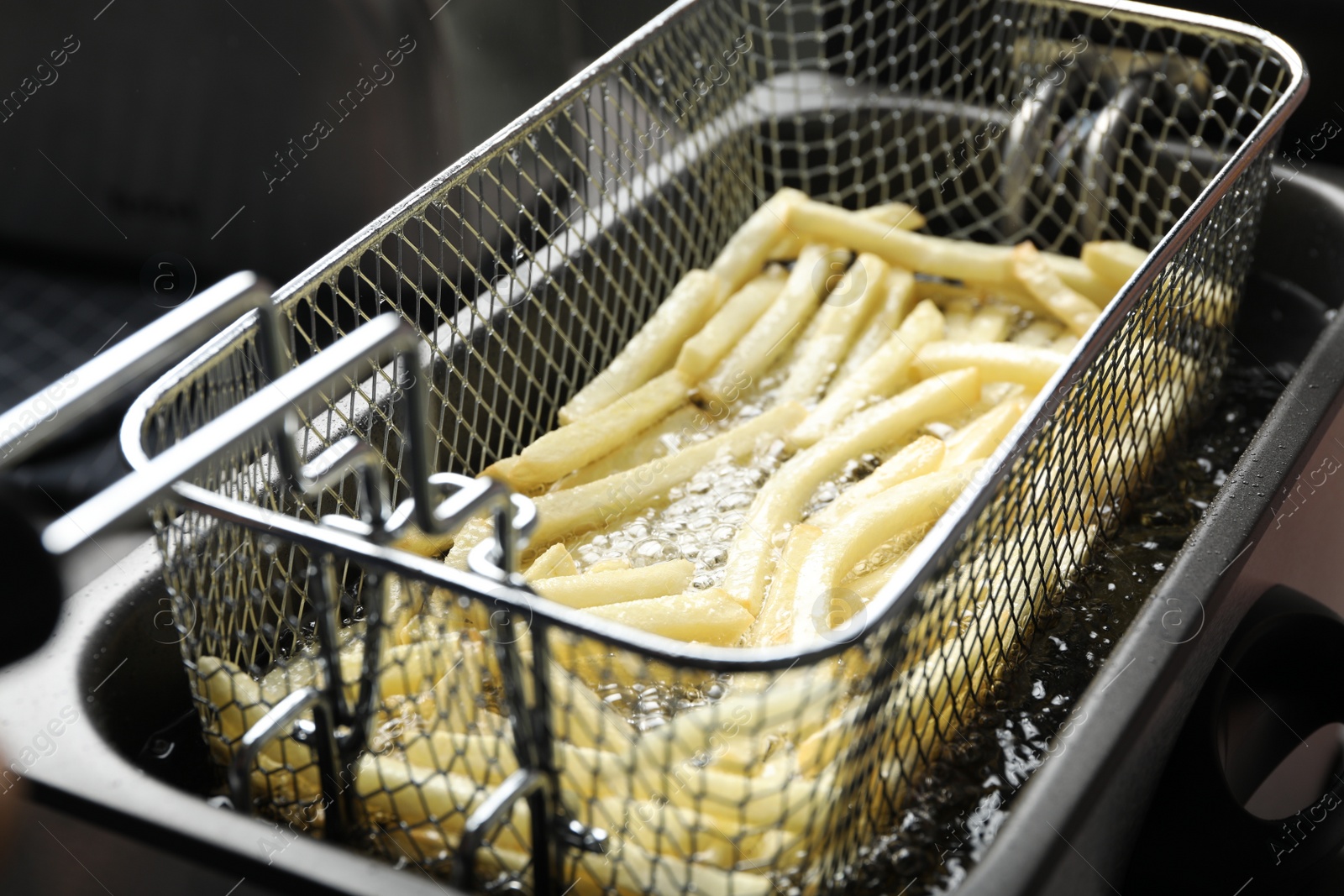 Photo of Cooking delicious french fries in hot oil, closeup