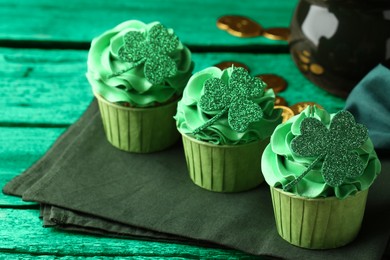 Image of St. Patrick's day. Tasty cupcakes with clover leaf toppers and cream on green wooden table, closeup