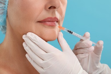 Photo of Doctor giving lips injection to senior woman on light blue background, closeup. Cosmetic surgery