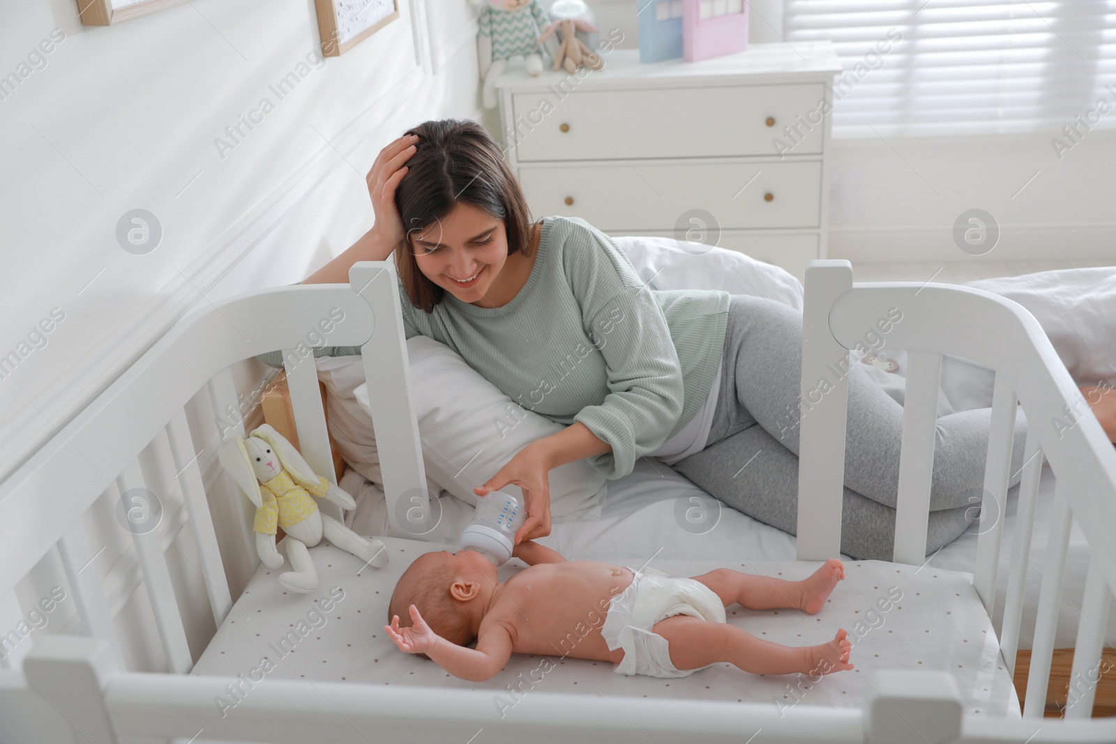 Photo of Happy young mother feeding her newborn baby from bottle at home