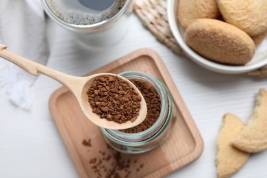 Spoon of instant coffee over jar on white table, top view