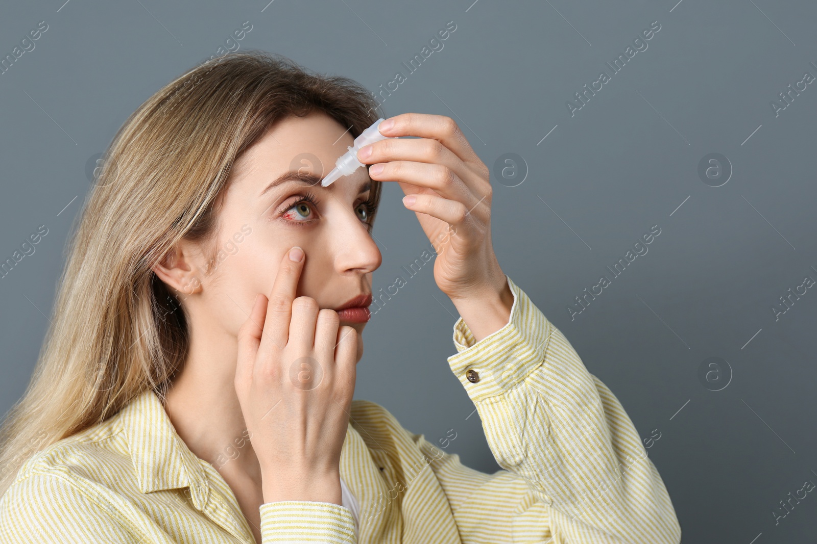 Image of Woman using eye drops on dark grey background